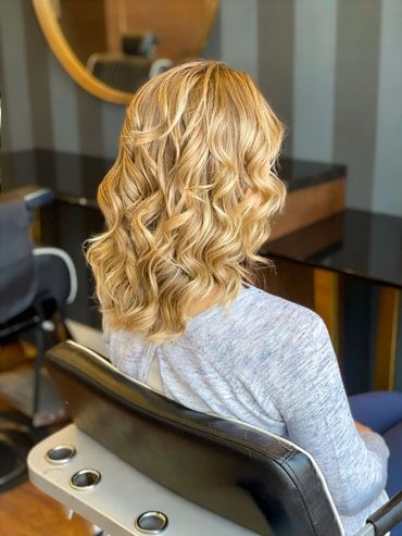 Soft blonde balayage with loose waves styled at Santoro Hair Salon in Brighton. The layered cut and 