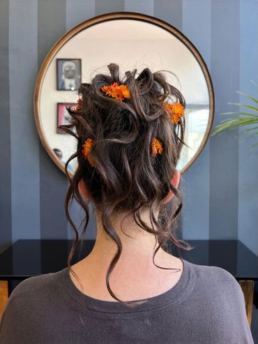 Creative updo with loose curls and orange flower accents, styled at Santoro Hair Salon in Brighton. 