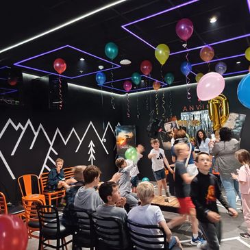 Children celebrating a birthday party with balloons and decorations indoors.