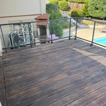 Terrasse en bois avec garde-corps en verre et vue sur le jardin.