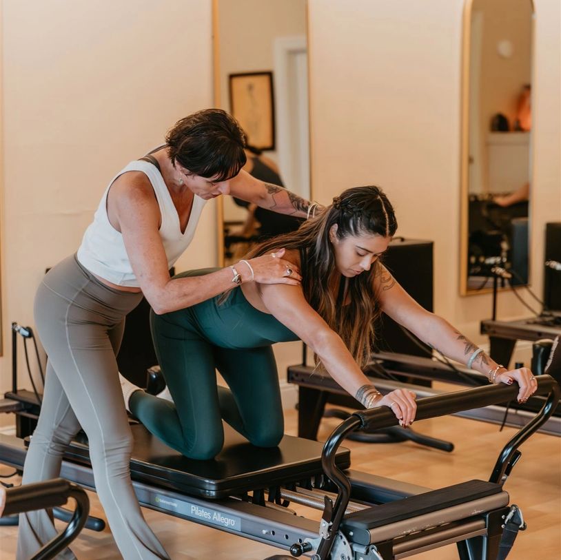 A Pilates instructor guides a woman using a reformer machine during a workout session.