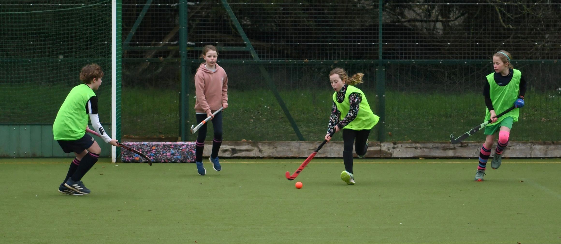 Children playing field hockey on an outdoor turf field.