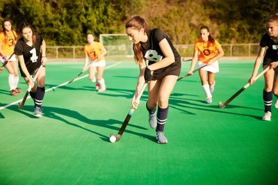 Girls playing field hockey on a sunny day.