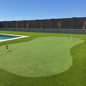 Backyard putting green next to a swimming pool under clear blue sky.