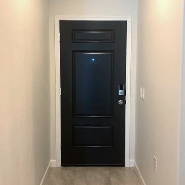 A sleek black door at the end of a narrow hallway with light-colored walls and tiled floor.