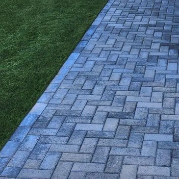 A neatly paved pathway beside a green grass lawn.