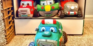 Stuffed toy trucks with smiling faces arranged on a shelf and floor.