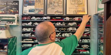 A man arranges a large collection of toy trucks on shelves.