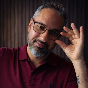 Smiling man adjusting his glasses, wearing a maroon shirt.
