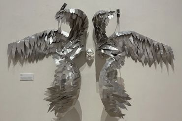 Metal sculpture of wings and a human face.