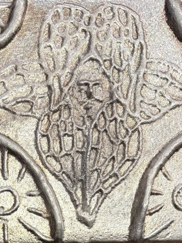 Carved angel figure with wings on a metallic surface.