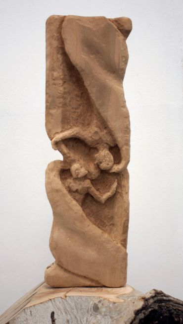 Abstract wooden sculpture with figures and draped shapes.