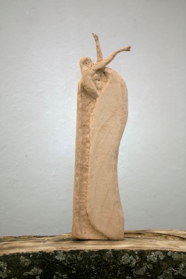 Abstract wooden sculpture resembling a figure with raised arms.