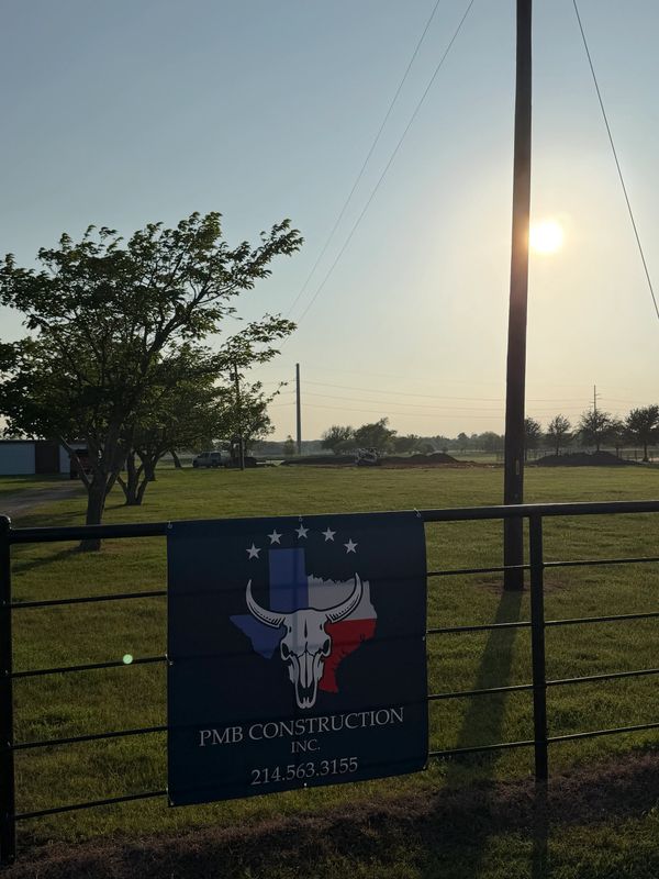 Sign for PMB Construction with Texas-themed logo on a fence at sunset.