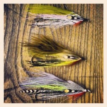 Three handcrafted fishing flies on a wooden surface.