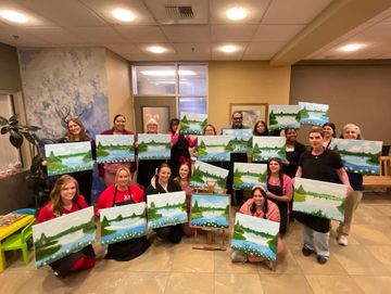 Group holding landscape paintings in a room.