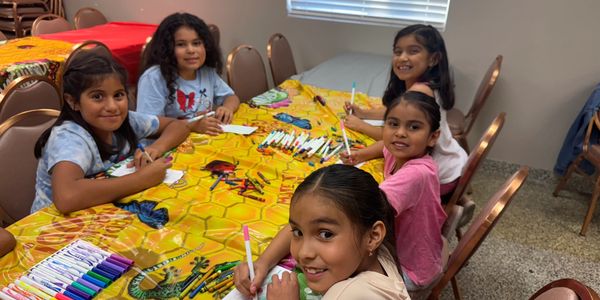 Five young girls happily coloring at a table with vibrant markers.