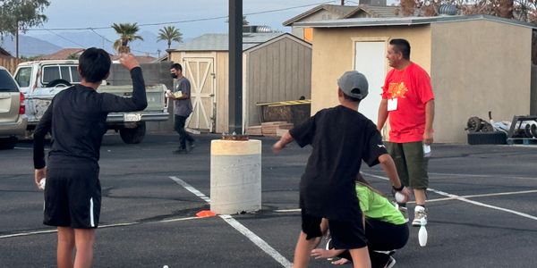 Kids and an adult play with juggling clubs in an outdoor parking lot.