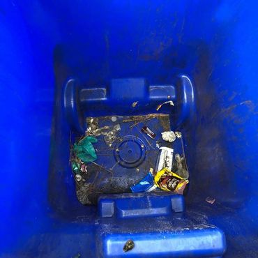Inside of a blue trash bin with some scattered trash.