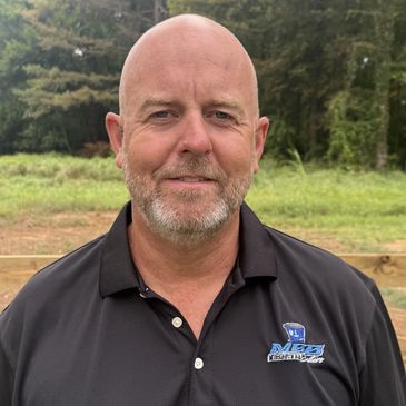 Bald man with beard wearing a black polo shirt outdoors.