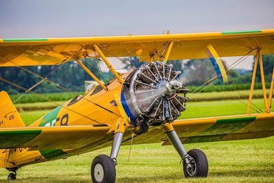 Yellow vintage biplane parked on grass with spinning propeller.
