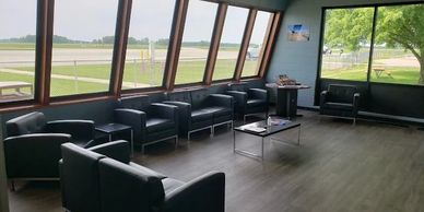 Modern waiting room with black chairs and large windows overlooking a runway.