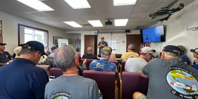 A group listens to a speaker in a meeting room filled with aviation decor.
