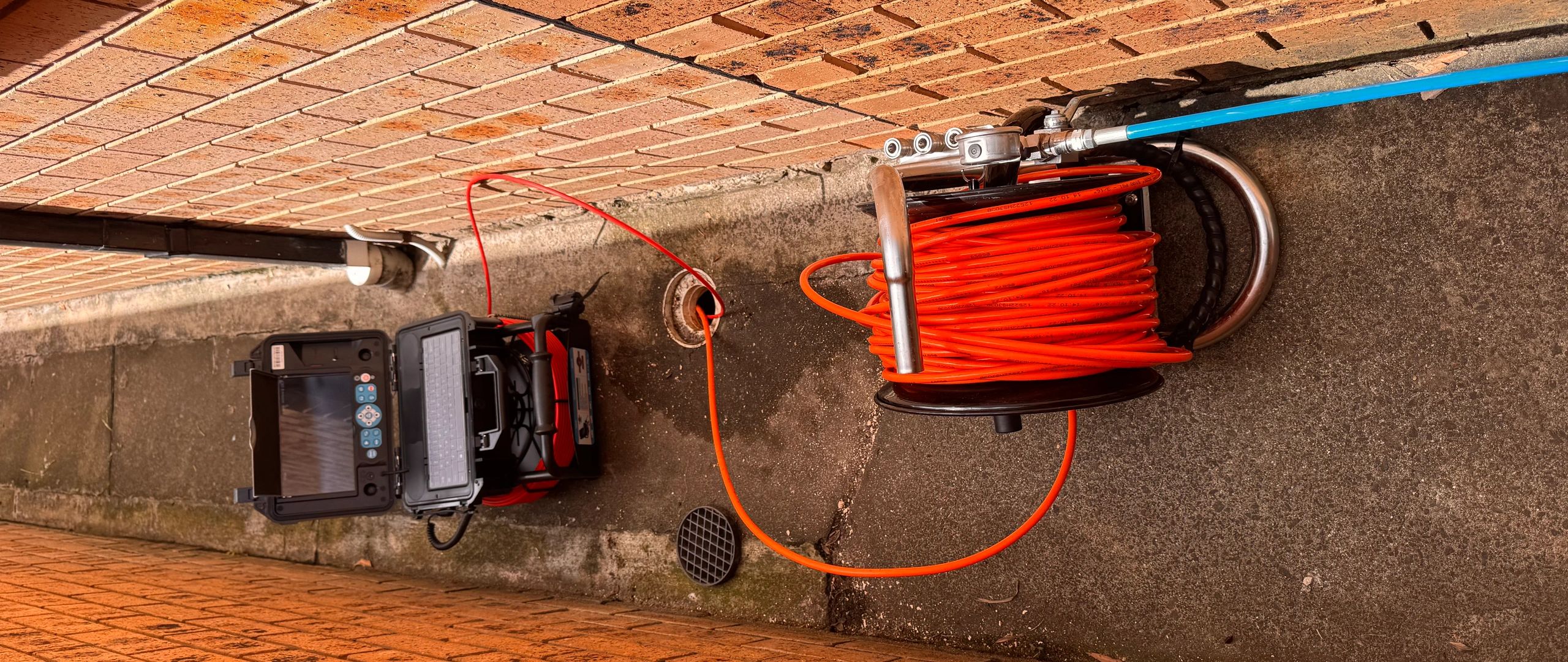Inspection camera setup with a coiled orange cable in narrow alley.