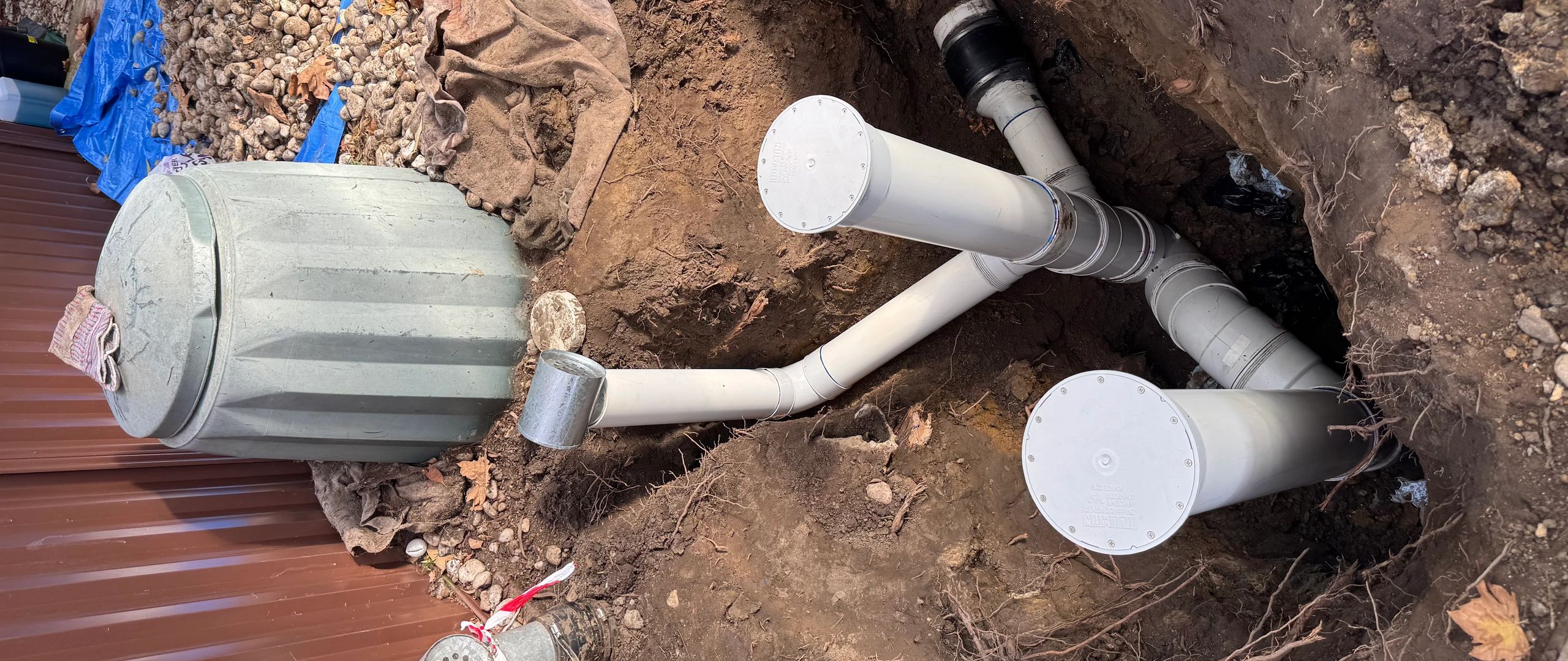 Outdoor septic system with exposed PVC pipes and a large gray tank.