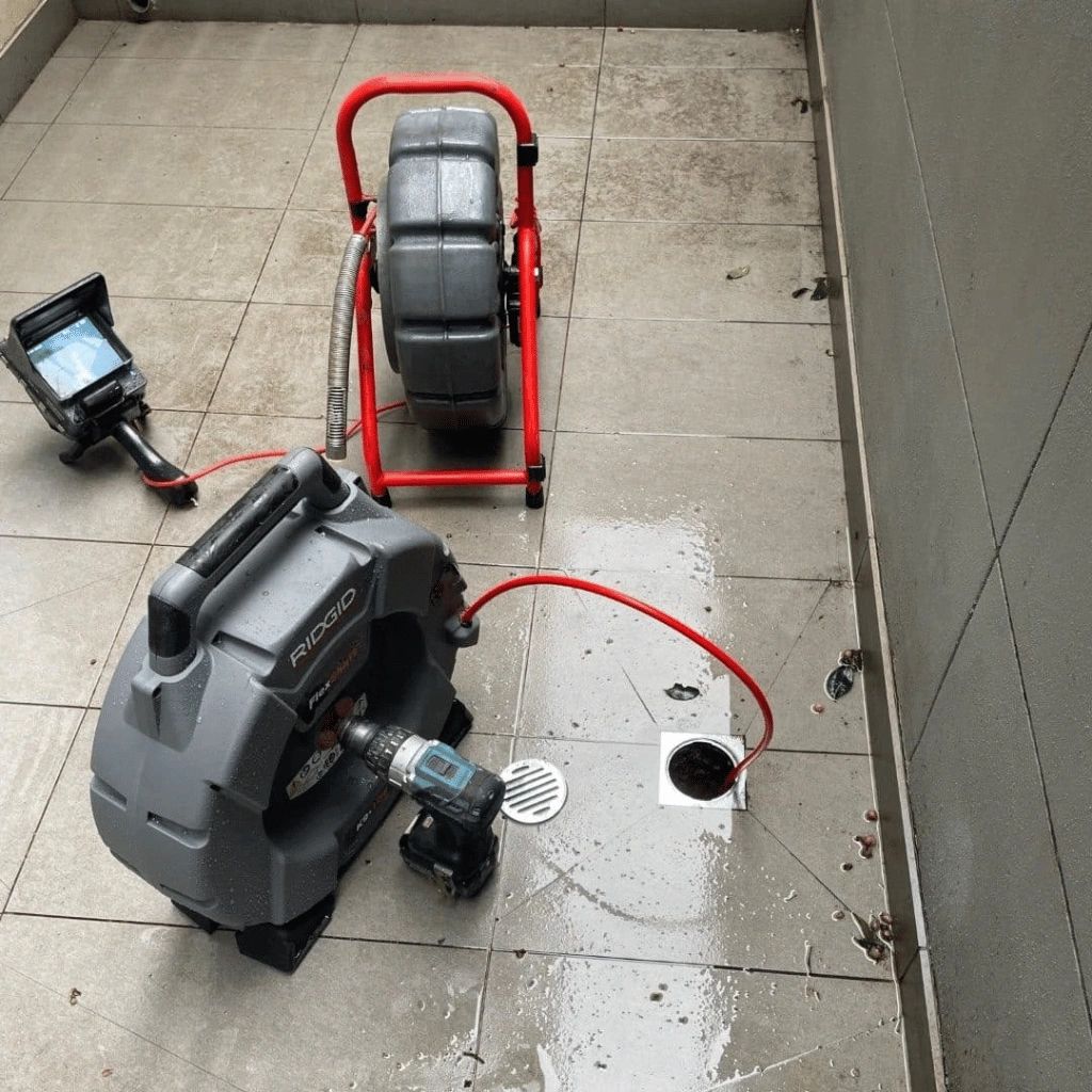 Drain cleaning machine with a monitor and red cable on tiled floor.