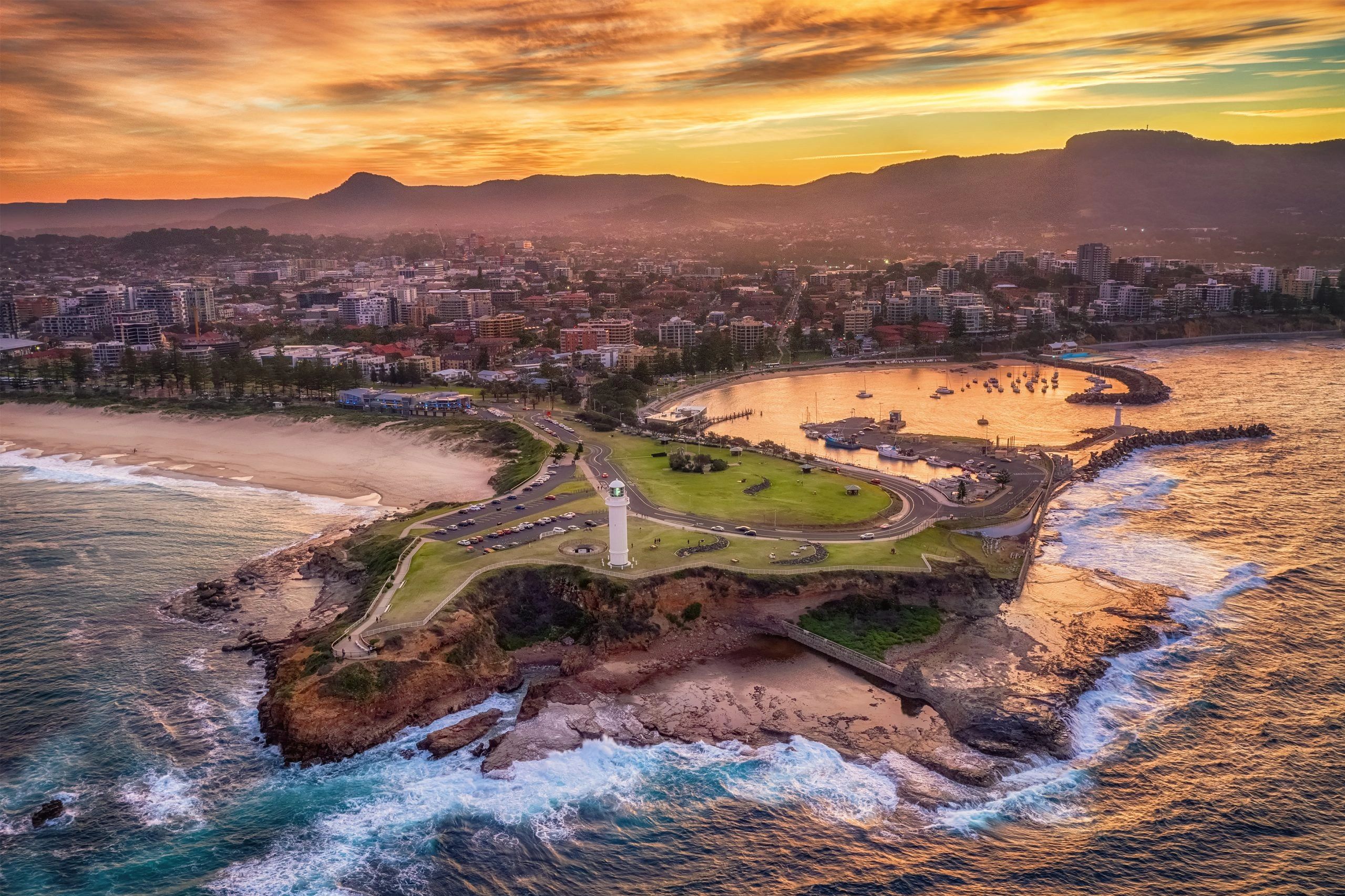 Sunset over a coastal city with a lighthouse and harbor.