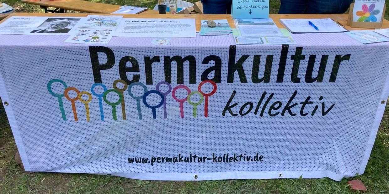 Informational booth for Permakultur Kollektiv with flyers and posters on a table.