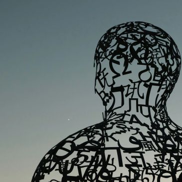 Sculpture made of letters and symbols against a clear sky.