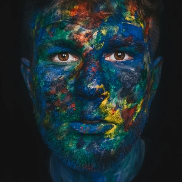 Man's face covered in vibrant blue, green, red, and yellow paint.
