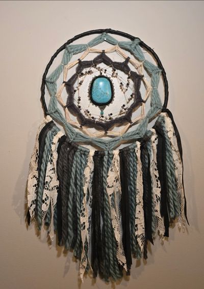 Handcrafted dreamcatcher with teal, cream, and gray yarn and lace details.