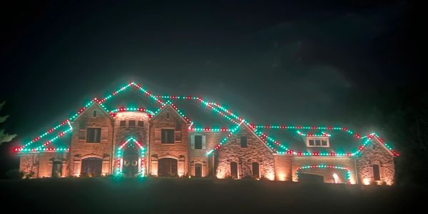 Large house decorated with red and green Christmas lights at night.