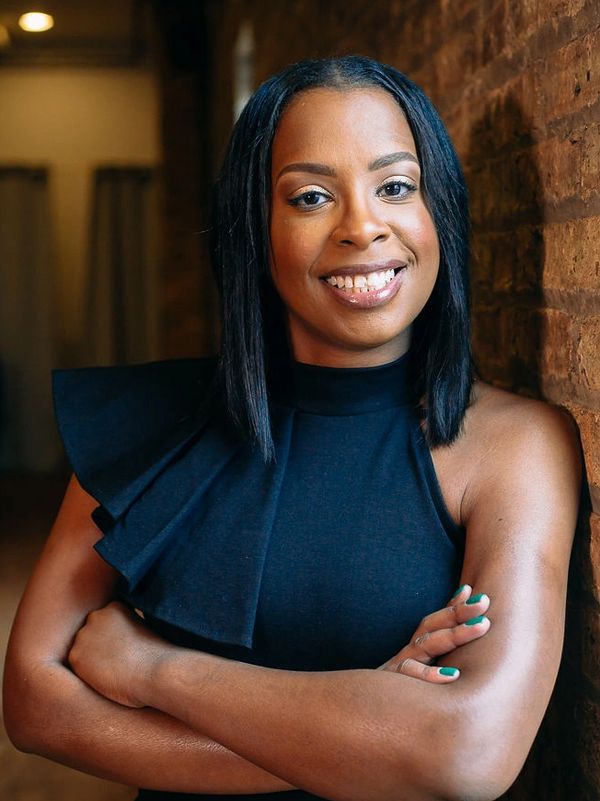 Confident woman with crossed arms smiling by a brick wall.
