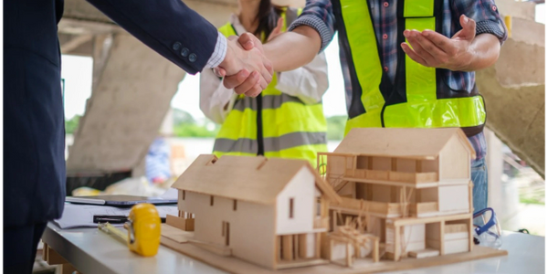 Construction workers shaking hands over house models on a table.