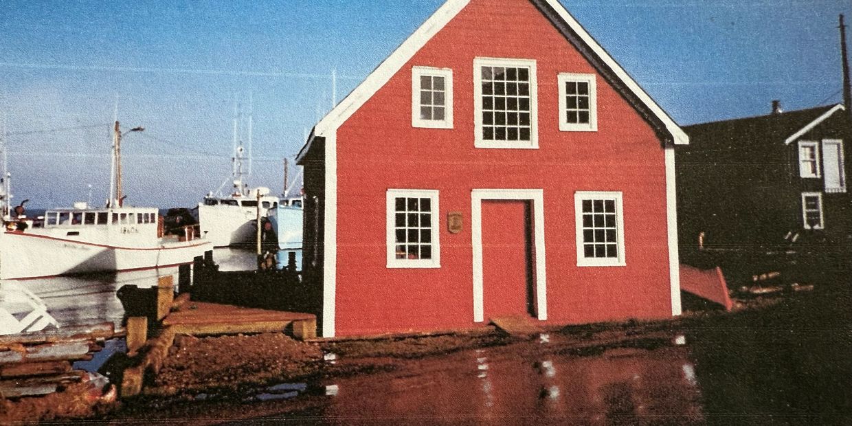 A red house with white trim near a dock and boats under a clear blue sky.