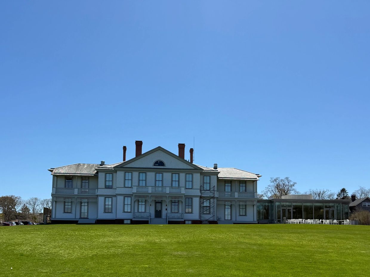 Large white house on a green lawn under clear blue sky.