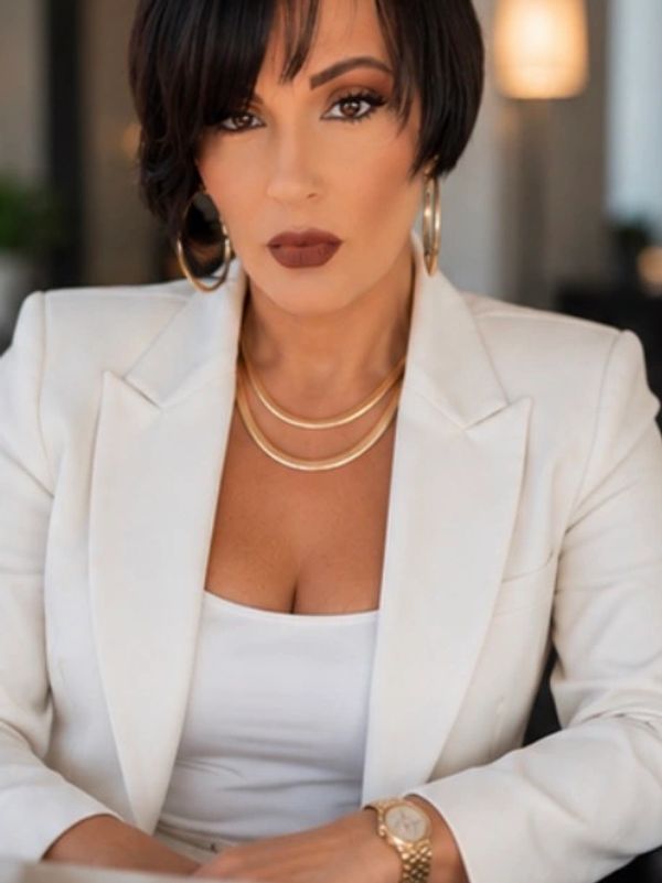 Confident woman in white blazer and gold jewelry.