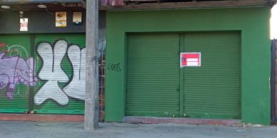 Green storefront with closed shutters and graffiti on adjacent walls.