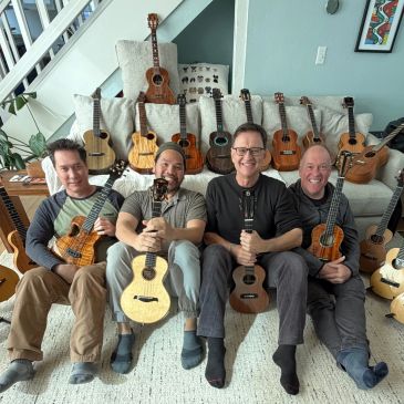 Four men sitting with multiple ukuleles around them.