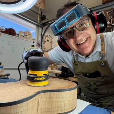 Man smiling while sanding a wooden guitar body.