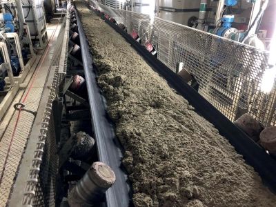 Industrial conveyor belt carrying a thick, grayish material.