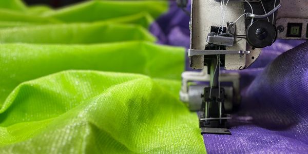 Close-up of sewing machine stitching green and purple fabric.
