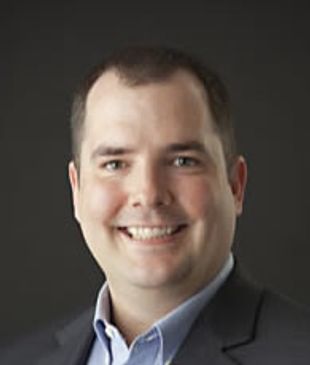 Professional man in business attire smiling against a dark background.