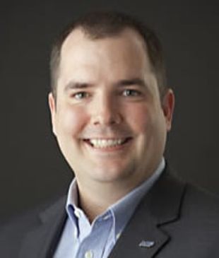 Professional man in business attire smiling against a dark background.