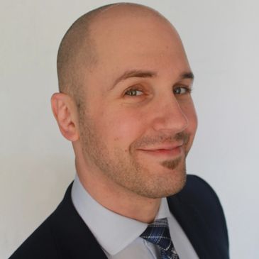 Smiling bald man in a suit and tie posing against a plain background.