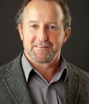 Portrait of a middle-aged man in a gray blazer and shirt against a dark background.